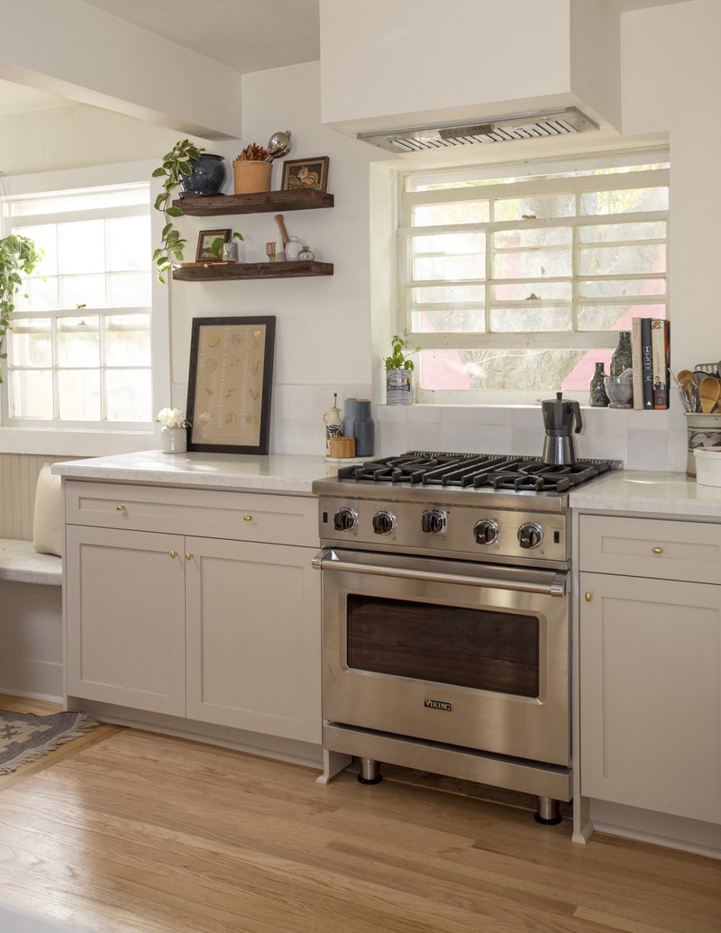 Viking range, warm gray kitchen cabinets with brass hardware, ventilation hood above window